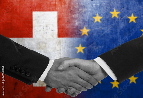 Two men/politicians in suits shaking hands with the national flags on the background - Switzerland and European Union