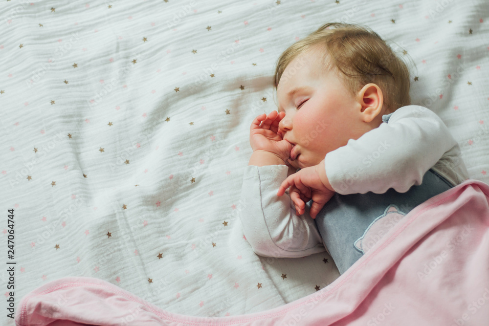 Φωτογραφία Infant baby sleeping and sucking thumb on white sheets