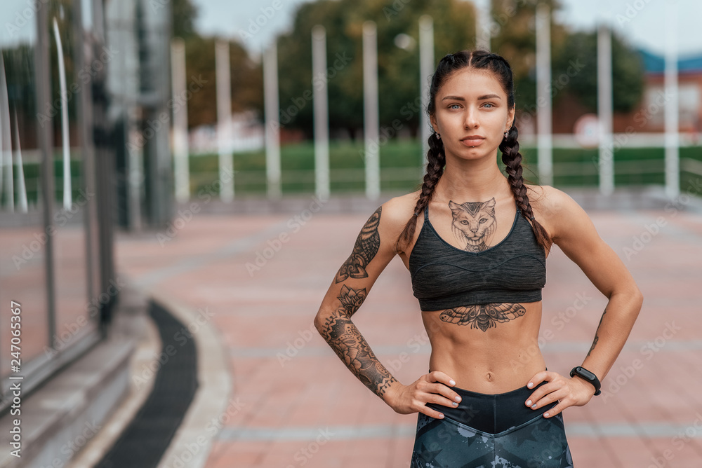Girl athlete, summer city. Resting after playing sports on the street. In  leggings and swimsuit. Woman with tattoos. Free space for text. Confident  look. Emotions of a strong and confident person. Stock