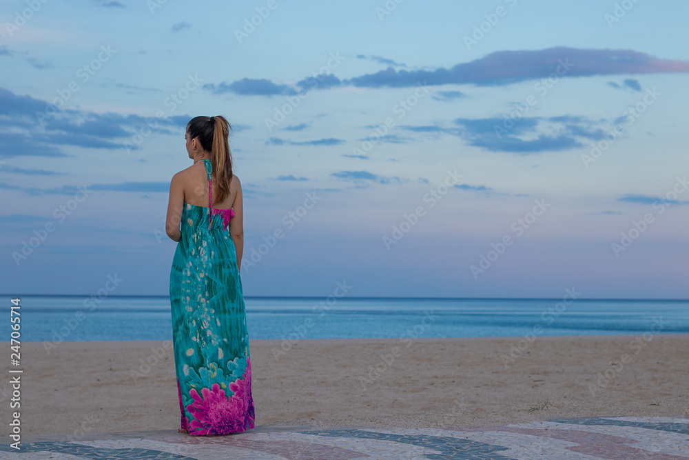 Beautiful younggirl with colorful dress poses in front of the sea. Blue sky and sea at summer. Elegance Beautiful younggirl with colorful dress poses in front of the sea. Blue sky and sea at summer. Elegance