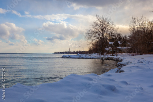 Toronto, CANADA - January 27th, 2019: Panoramic Canadian winter landscape near Toronto, beautiful frozen Ontario lake at sunset. Scenery with winter trees, water and blue sky.
