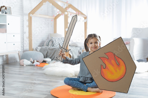 Cute little girl playing with cardboard armor in bedroom