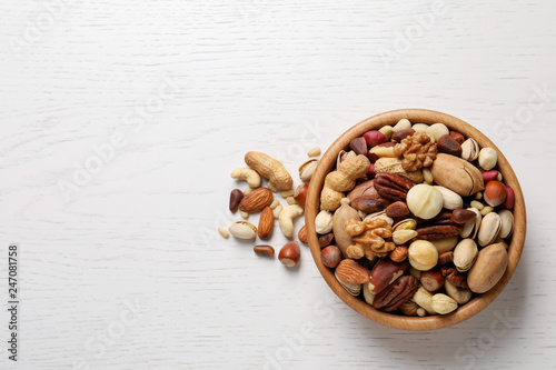 Bowl with organic mixed nuts on white wooden background, top view. Space for text