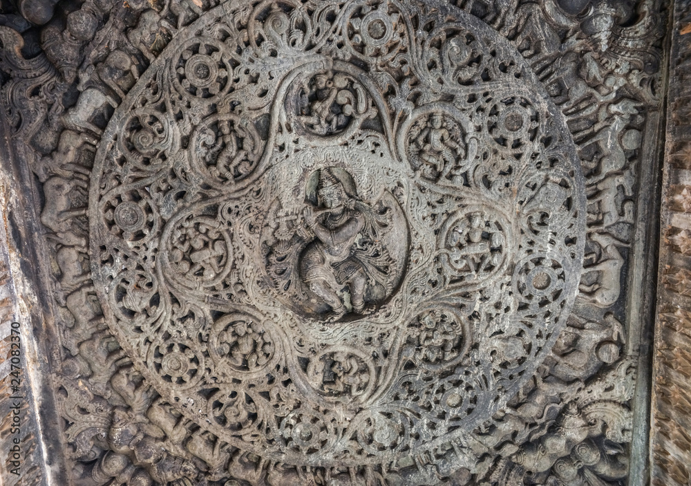 Belavadi, Karnataka, India - November 2, 2013: Veera Narayana Temple. Gray stone Sculpture set in circular mandala on ceiling of Mandapam shows flute playing god Krishna surrounded by dancing girls an
