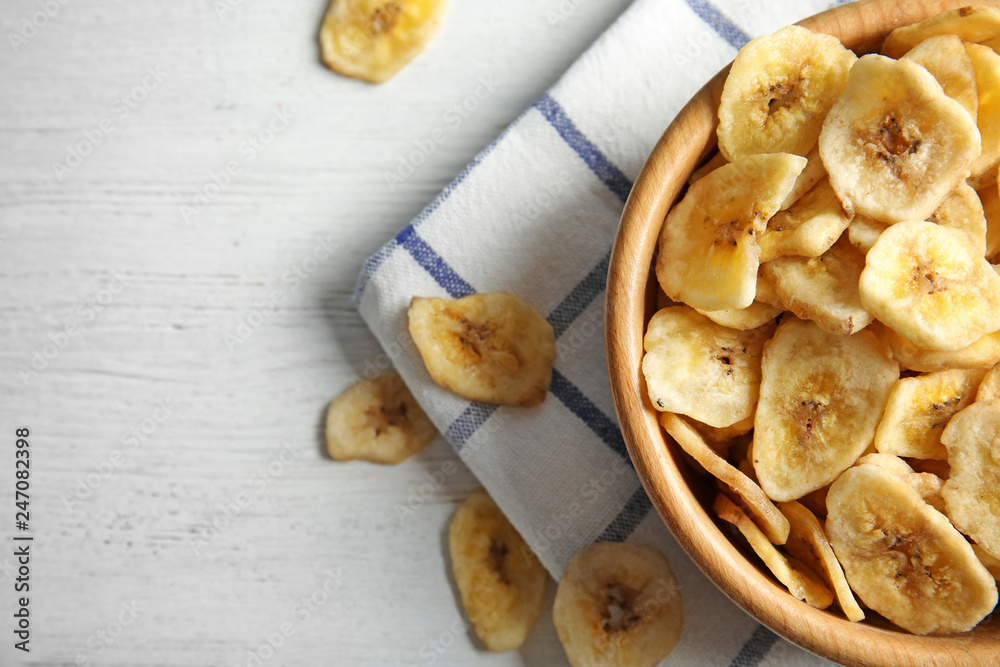 Wooden bowl with sweet banana slices on table, top view with space for text. Dried fruit as healthy snack