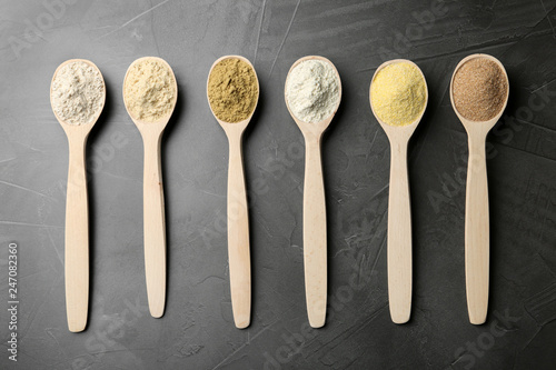 Spoons with different types of flour on grey background, top view