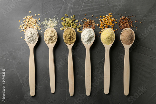 Spoons with different types of flour and ingredients on grey background, top view