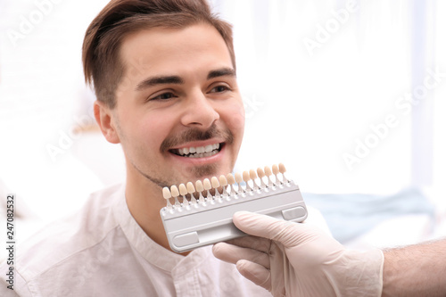 Dentist checking young man's teeth color in dental office