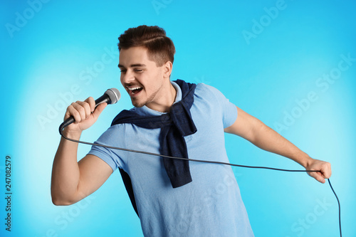 Young handsome man in casual clothes singing with microphone on color background