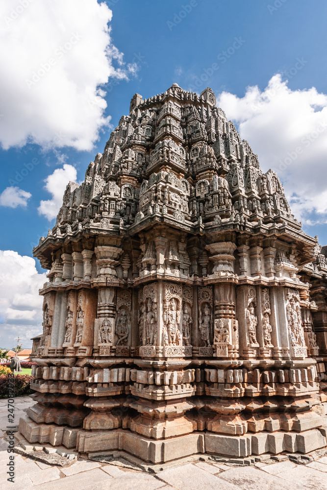 Belavadi, Karnataka, India - November 2, 2013: Veera Narayana Temple. Closeup of the wiht statues heavy decorated tower on one of three brown-stone Vimanams of the complex under cloudscape. 