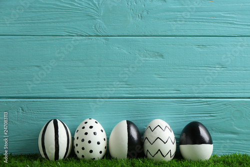 Line of painted Easter eggs on green lawn against wooden background, space for text