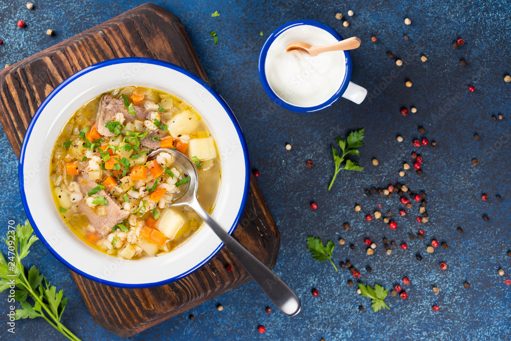 Rassolnik - Traditional Russian soup with pickled cucmbers, pearl barley, meat, pickles, carrots and potatoes on blue background. Top view