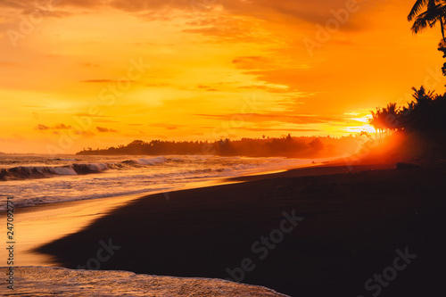 Bright sunset or sunrise with ocean waves and coconut palms in Bali  Keramas beach