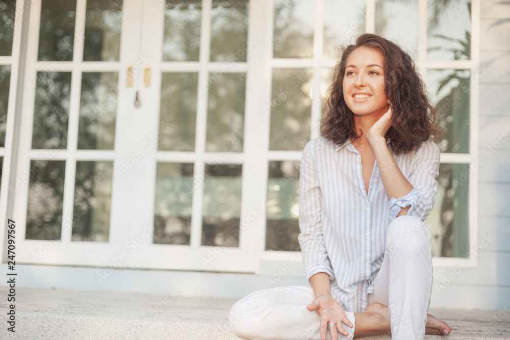 Portrait of a beautiful young woman with dark hair sitting on the terrace of her house with panoramic windows