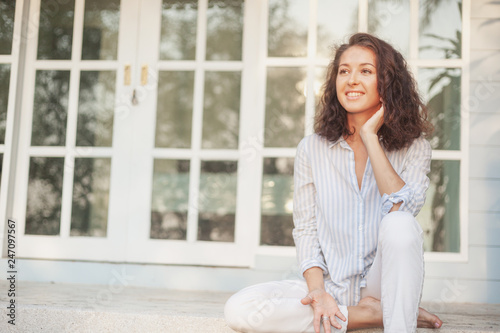 Portrait of a beautiful young woman with dark hair sitting on the terrace of her house with panoramic windows