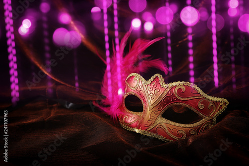 Photo of elegant and delicate gold, red venetian mask over dark velvet and silk background.