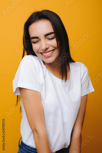 Close up portrait of a lovely european shy woman smiling with closed eyes against a yellow background.
