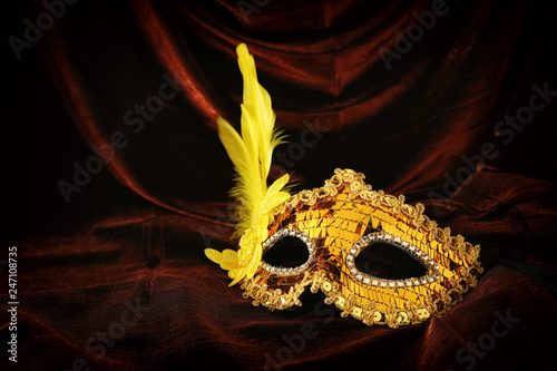 Photo of elegant and delicate gold venetian mask over dark velvet and silk background.