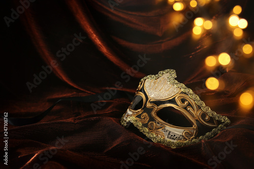 Photo of elegant and delicate gold venetian mask over dark velvet and silk background.