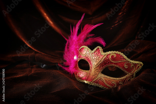 Photo of elegant and delicate gold, red venetian mask over dark velvet and silk background.