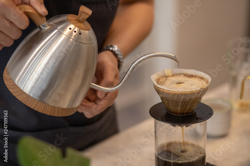 Barista Brewing Drip Coffee, Hand Pouring Hot Water from The Kettle over The Coffee Powder.  Close up © Semachkovsky 