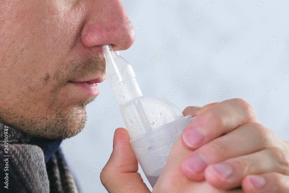 Sick man inhaling through inhaler nozzle for nose. Close-up nose, side view. Use nebulizer and inhaler for the treatment. Sick man inhaling through inhaler nozzle for nose. Close-up nose, side view. Use nebulizer and inhaler for the treatment.