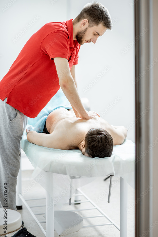 Obraz premium Young male therapist doing back massage to a man lying in the white cabinet of the rehabilitation clinic