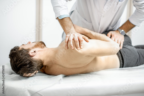 Professional senior physiotherapist doing manual treatment to a man in the cabinet of rehabilitation clinic