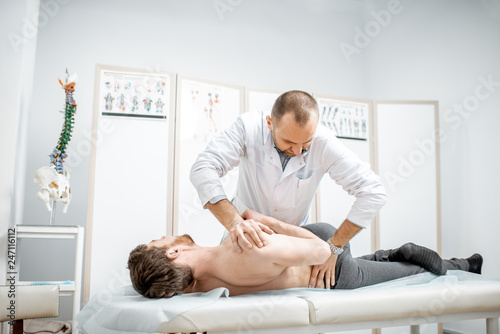 Professional senior physiotherapist doing manual treatment to a man in the cabinet of rehabilitation clinic photo