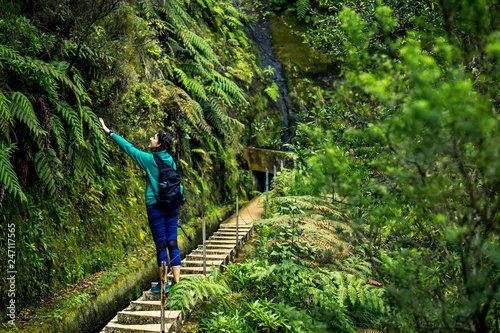 Portrait of young girl in green sweatshirt walking by levana on Madeira island  up in mountains. Hiking by the trail among green  tropical and old forests. Portugal.