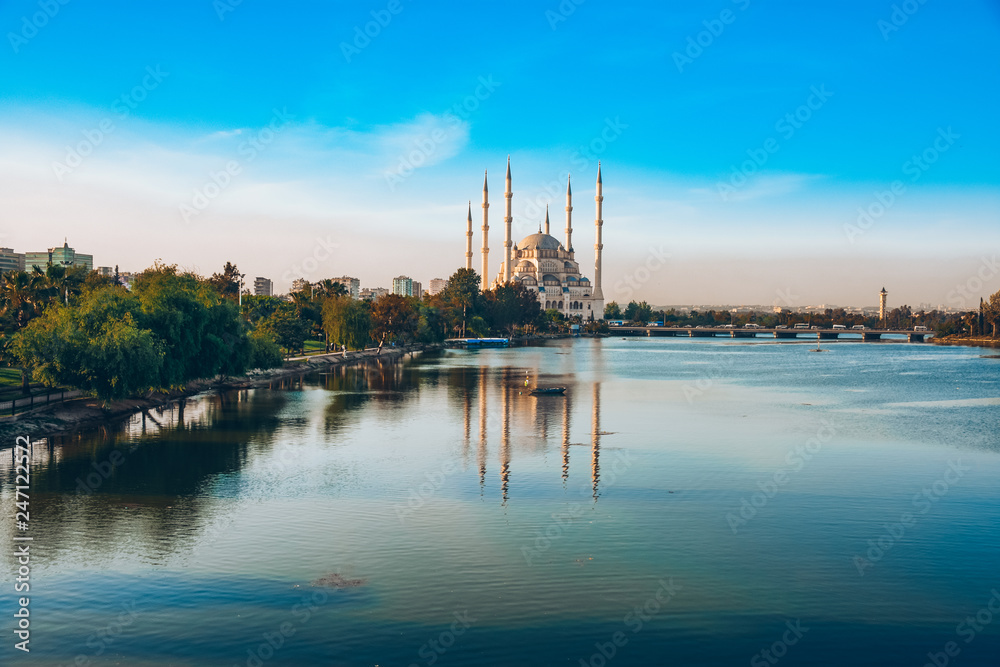 City of Adana, Turkey. Sabanci Central Mosque in Adana with Seyhan River and Trees. Mosque has reflections from Seyhan river in sunny day with blue clean sky