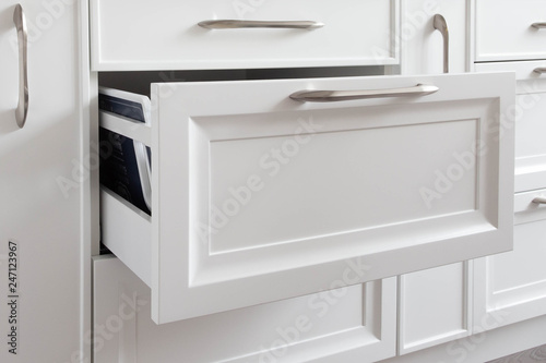 Opened drawer on a white black classic traditional kitchen with kitchen utensils inside. 
