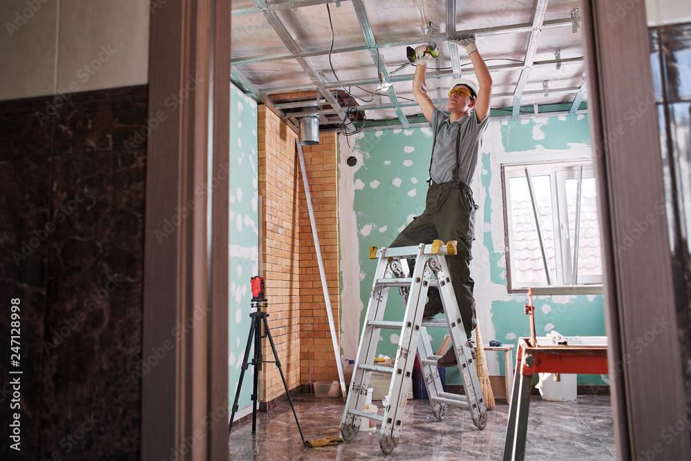 Room repair. Interior finish. young builder makes a plasterboard ceiling, standing on a stepladder Room repair. Interior finish. young builder makes a plasterboard ceiling, standing on a stepladder