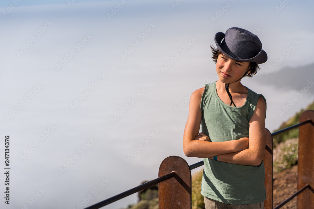 Portrait of a boy in a hat and t-shirt on top of the mountain.