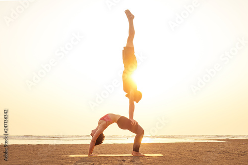 two young man and beautiful woman on beach doing fitness yoga exercise together. Acroyoga element for strength and balance at sea octan goa india sunset