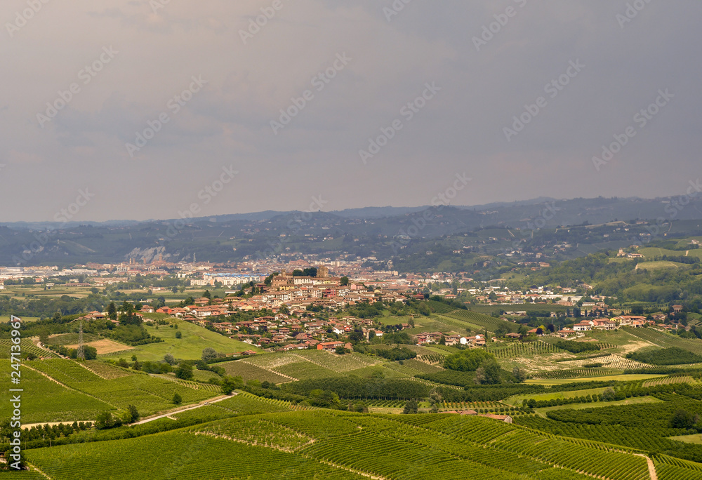 Panoramic view of hills and valleys with a medieval village and cloudy sky in springtime, Roddi d'Alba, Langhe, Piedmont, Italy
