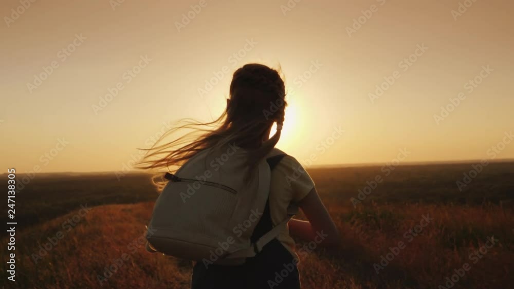 A long-haired child with a backpack runs towards the sun. Children's dreams and vacations concept A long-haired child with a backpack runs towards the sun. Children's dreams and vacations concept
