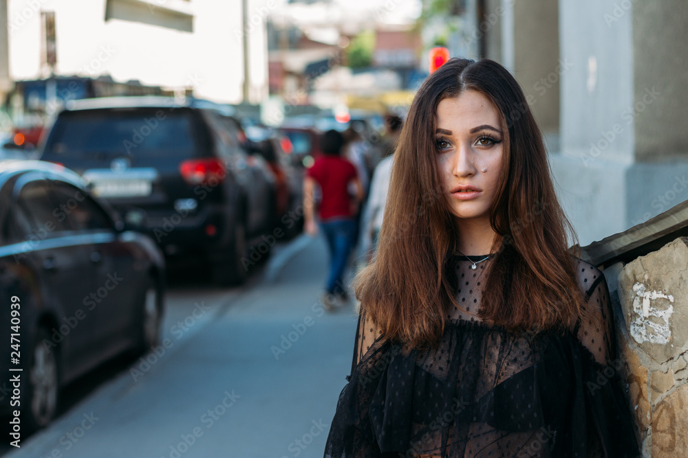 portrait of a girl, brunette, in a black dress, in the arch, in the city. posing, walking. alone in the crowd, loneliness