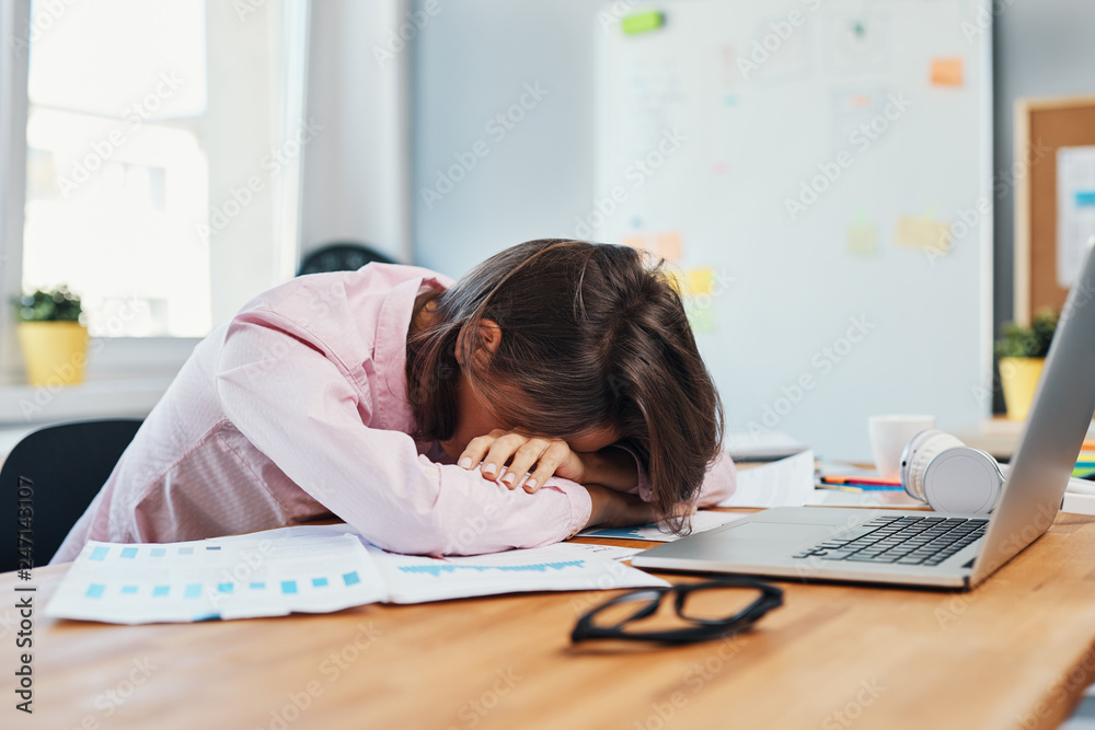 Stressed young woman resting head on desk overwhelmed by work Stock