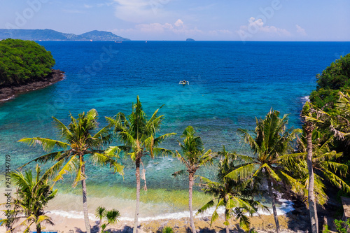 Aerial view of a tropical beach with palm trees and coastline and the boat sways on the water of the ocean. Rainforest, blue lagoon on the island of Bali