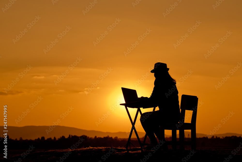 Obraz premium Silhouette a beautiful woman is working on a notebook at sunset.