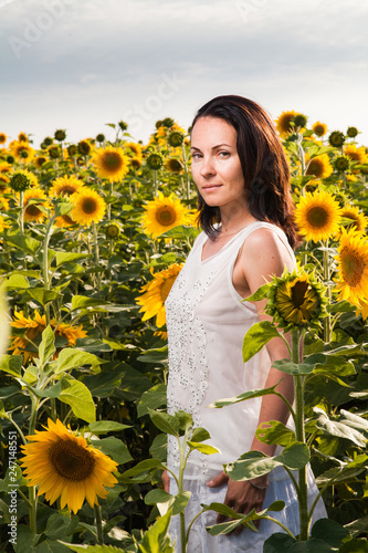 half turn portrait of brunette girl in white blouse in sunflower field on summer Sunny day