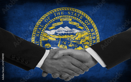 Two men/politicians in suits shaking hands with the national flag on the background - Nebraska - United States photo