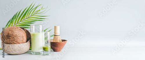 Matcha latte drink with coconut milk on table with whole coconut , matcha espresso and macha whisk, front view, banner. Healthy detox nutrition, vegan food and clean eating concept. Copy space, banner