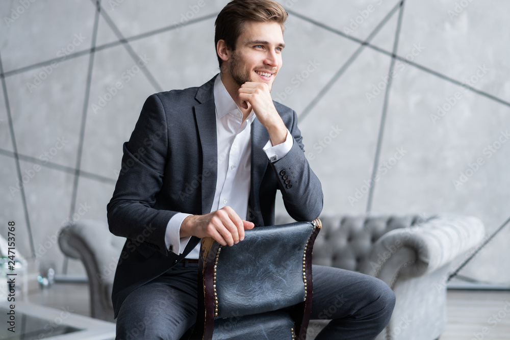 Portrait of confidence. Thoughtful young man in full suit looking away while sitting on the stool. Portrait of confidence. Thoughtful young man in full suit looking away while sitting on the stool.