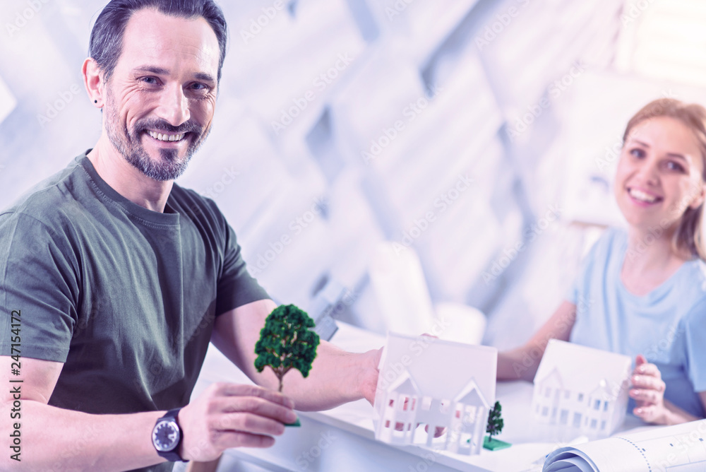 Handsome man smiling while visiting real estate agent and holding tree miniature Handsome man smiling while visiting real estate agent and holding tree miniature