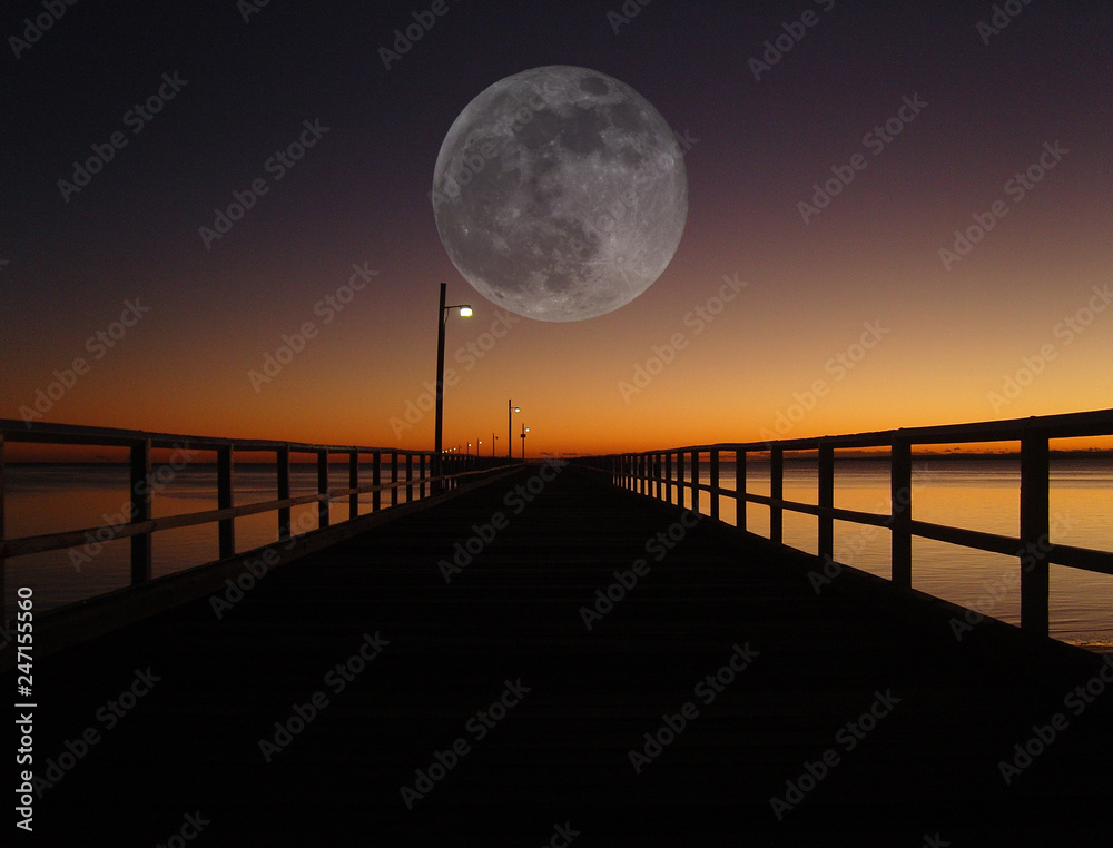 Full moon rising above a fishing pier at sunrise/sunset