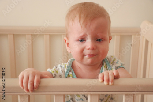 Sad first year baby is crying in his bed. Growing teeth acke