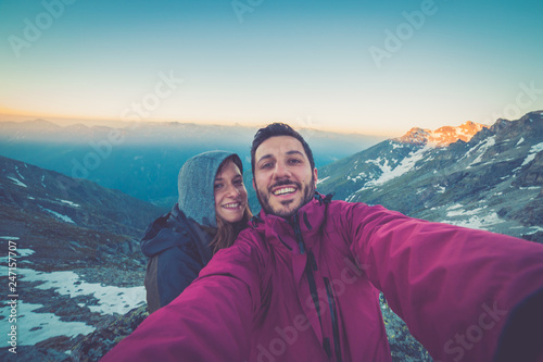 Couple of hikers taking selfie from top of the mountain with peaks and valley view on the background after long trekking