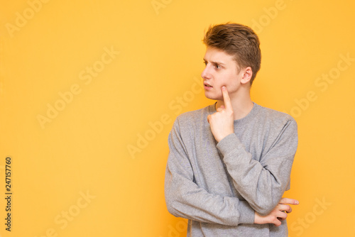 Handsome young man in casual clothing is on a yellow background and looks to the side. Thoughtful guy looks out to the side, isolated on a yellow background.